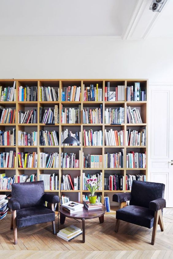 a simple modern library with a large bookcase and black leather chairs plus a side table and a lamp