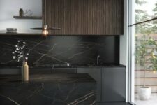 a sophisticated black kitchen with black and fluted stained cabinets, a black marble backsplash and a kitchen island, a pendant lamp