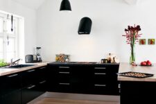 a stylish black contemporary kitchen with only lower cabinets, beige stone countertops, black pendant lamps and a black hood
