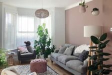 a stylish living room with dusty pink walls, a grey sofa, a grey chair, a white one, potted greenery