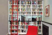 a stylish modern library with a large built-in bookcase unit, a built-in fireplace and a red curved chair and a red staircase