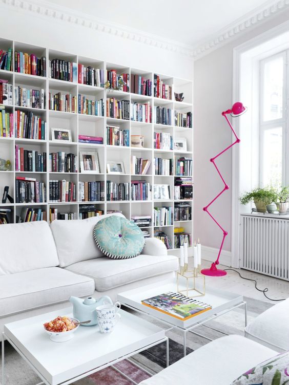 A stylish modern library with a large built in bookcase, white furniture and a whimsy hot pink floor lamp