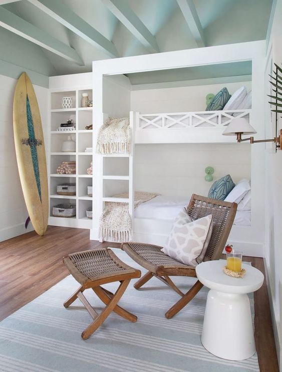 A surfer chic kids' room with white and stained furniture, neutral and pastel bedding, a surfing board, built in shelves and cool built in bunk beds