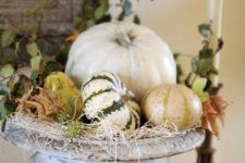 a vintage urn with hay, natural pumpkins and gourds and leaves is a cool centerpiece for the fall
