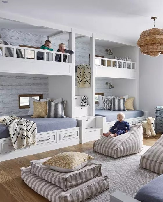 A welcoming beachfront grey kids' room with four built in bunk beds, grey and yellow bedding, cushions, pillows and beanbag chairs