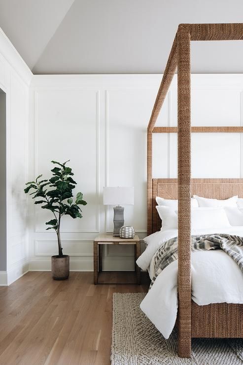 a welcoming bedroom with white walls with molding, a bed covered with jute, neutral textiles and a potted plant is cool