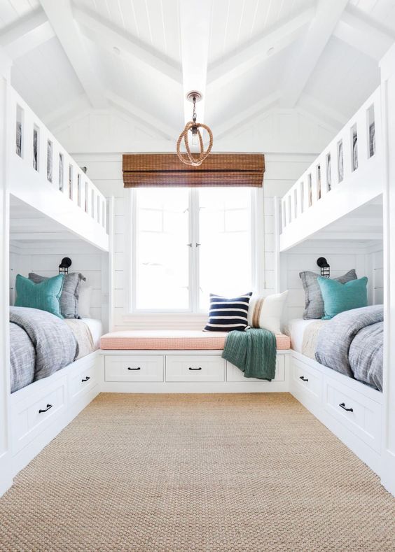 a white beach-inspired kids' room with built-in bunk beds, grey and aqua bedding, a windowsill bench and a woven rug