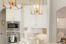 a white glam kitchen with white marble countertops, gold cage pendant lamps and neutral fixtures