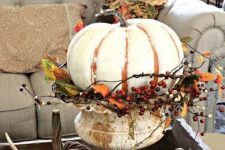 a white painted pumpkin with twigs and faux berries placed in a vintage urn as a stand for a shabby chic touch