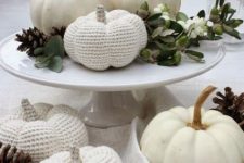 a white porcelain stand with greenery, berries, pinecones, natural and crochet white pumpkins