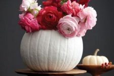 a white pumpkin on a wooden stand with red, fuchsia and pink blooms as a chic and bright fall centerpiece