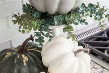 a white stand with eucalyptus and a chalk paint pumpkin plus more pumpkins under it for a rustic feel