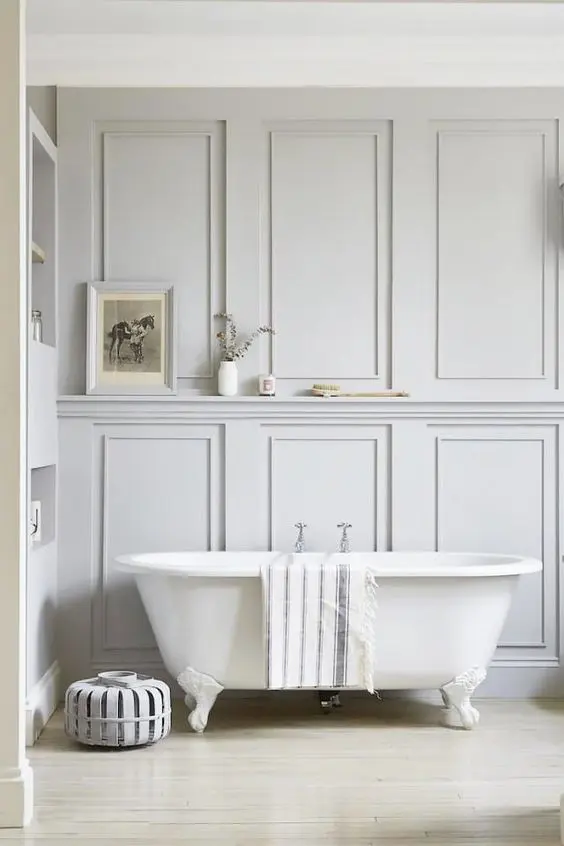 An airy bathroom with molding on the walls, a built in shelf, a refined clawfoot tub is a very calming and soothing space