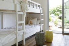 an airy kids’ bedroom with built-in bunk beds with white bedding, a yellow and a grey side table and a faux fur rug