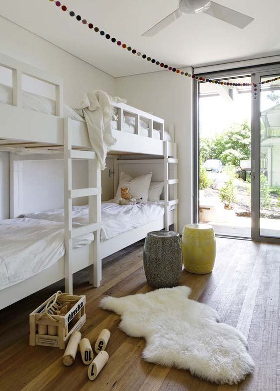 An airy kids' bedroom with built in bunk beds with white bedding, a yellow and a grey side table and a faux fur rug