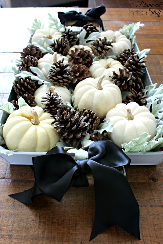 an elegant fall centerpiece of pale greenery, white pumpkins, pinecones and black silk bows
