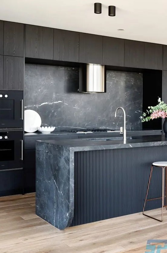 An exquisite kitchen with dark stained cabinets, a black fluted kitchen island, a black marble backsplash and countertops