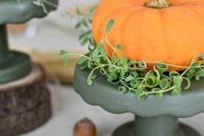 an orange pumpkin with greenery placed on a black stand is a bold and modern fall centerpiece