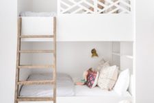 built-in white bunk beds with a wooden ladder, catchy railing, wall lamps and storage drawers in the lower bed