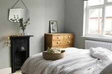 a Nordic bedroom with grey walls, a vintage built-in hearth, a bed with neutral and printed bedding, a stained dresser and a mirror