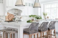 a beautiful modern kitchen with white shaker style cabinets, a large kitchen island with woven chairs and stools, pendant lamps