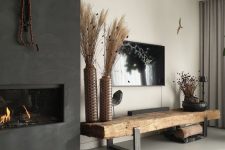 a boho monochromatic living room with a built-in fireplace, a rough wood bench, a TV on the wall and dried grass arrangements