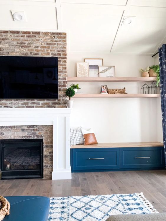 a brick clad fireplace with a built-in bench with drawers and some pillows plus built-in shelves over it