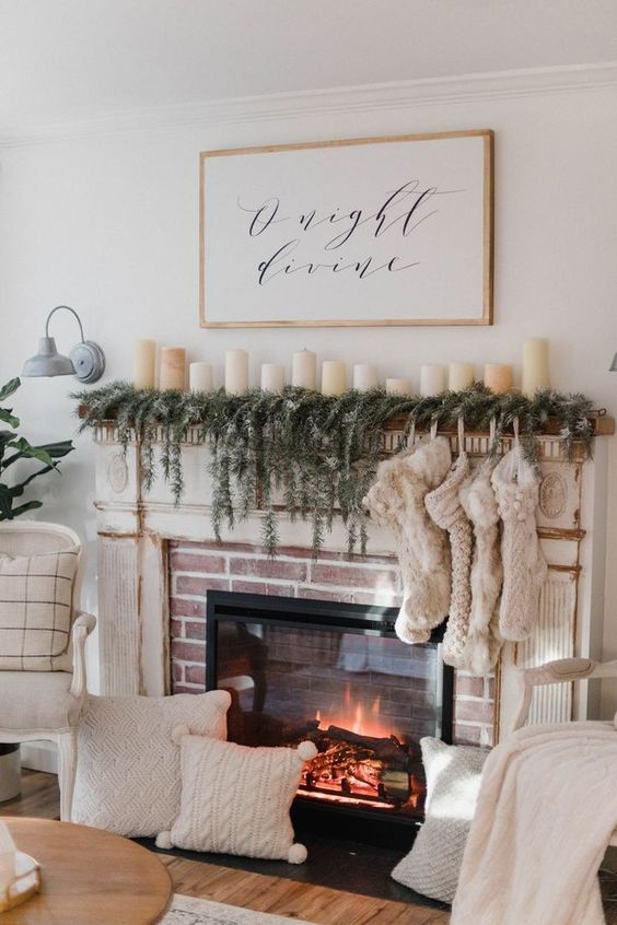 A built in fireplace with an evergreen garland, lot sof stockings and pillar candles on the mantel