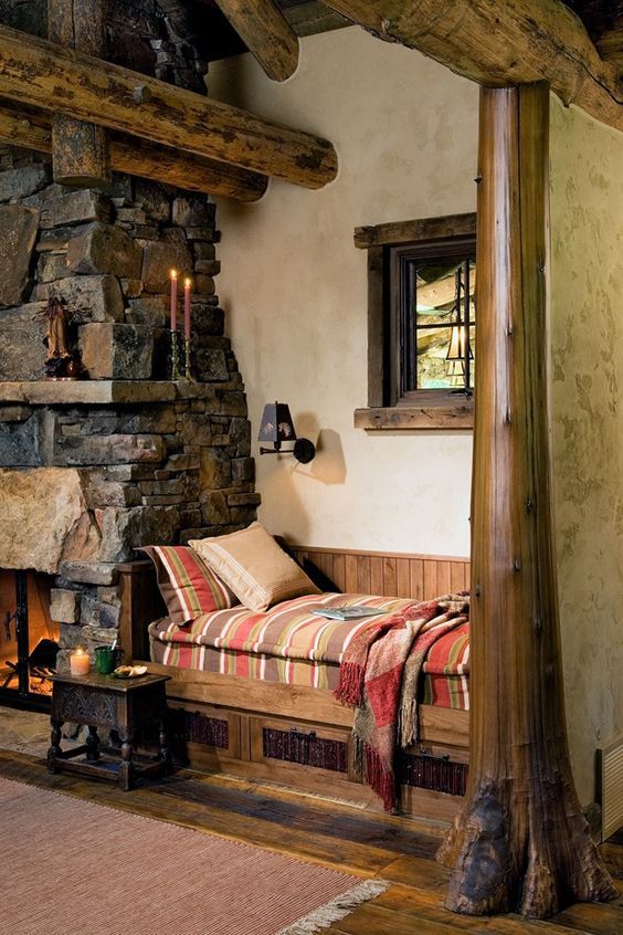 A chalet nook with a stone clad fireplace and a mantel, a built in wooden bench with drawers and bright bedding is welcoming