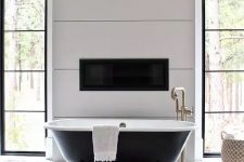 a chic vintage bathroom with white geo tiles, a black clawfoot bathtub, a built-in fireplace and a chic chandelier