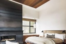 a contemporary bedroom with a natural feel, a metal fireplace, a stained wood ceiling, a wooden and rattan bed, a wooden desk and a grey chair
