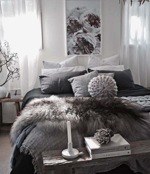 A cozy and moody bedroom with faux fur blankets, knit blankets and a rough wood bench is winter reayd and very trendy