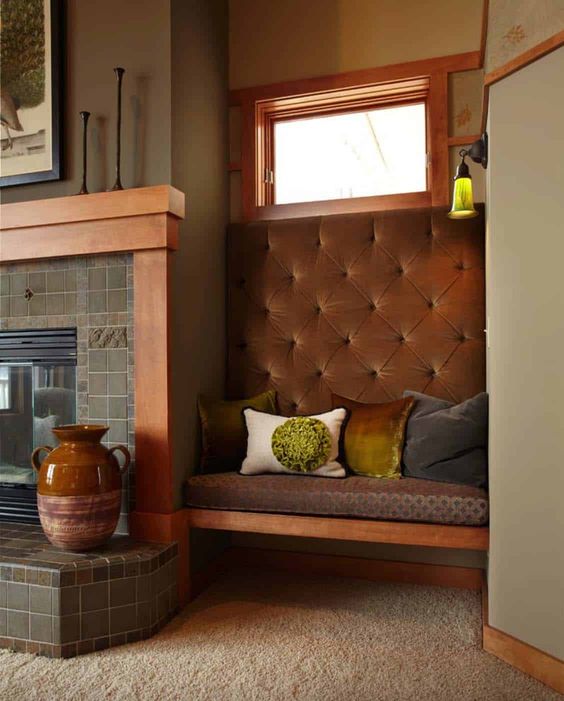 A cozy fireplace nook with a fireplace clad with green tiles and a built in bench with pillows and a bold vase is cool