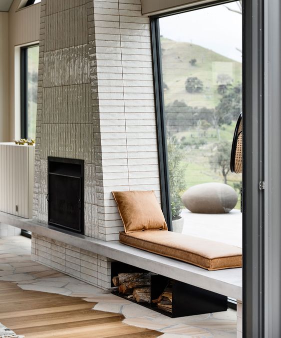 a creative modern fireplace clad with tiles, with a windowsill daybed with leather cushions and a firewood storage under it