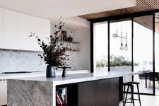 a fantastic minimalist kitchen with white cabinets, grey marble countertops and a backsplash, a black kitchen island with a waterfall countertop and black stools