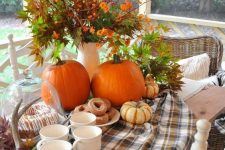 a farmhouse Thanksgiving tablescape with a plaid runner, leaves, pumpkins, greenery and berries in a vase and antlers