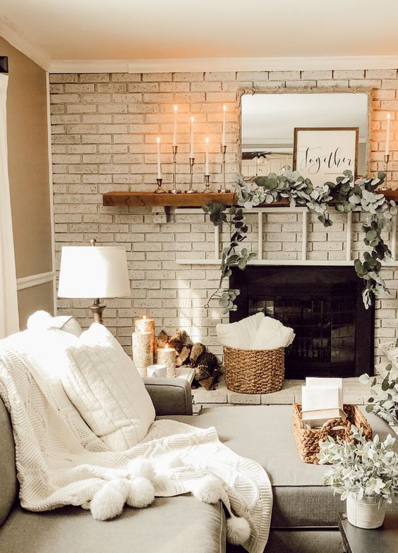 a fireplace deocrated with fresh greenery, candles and some firewood by its side for a cozy feel