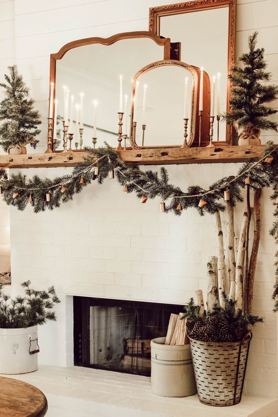 a fireplace styled with an evergreen garland with bells, lot sof candles and lots of mirrors