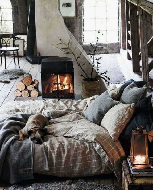 a gorgeous winter bedroom with plaid and knit bedding, a fur rug, a hearth and some firewood that make the space cozy