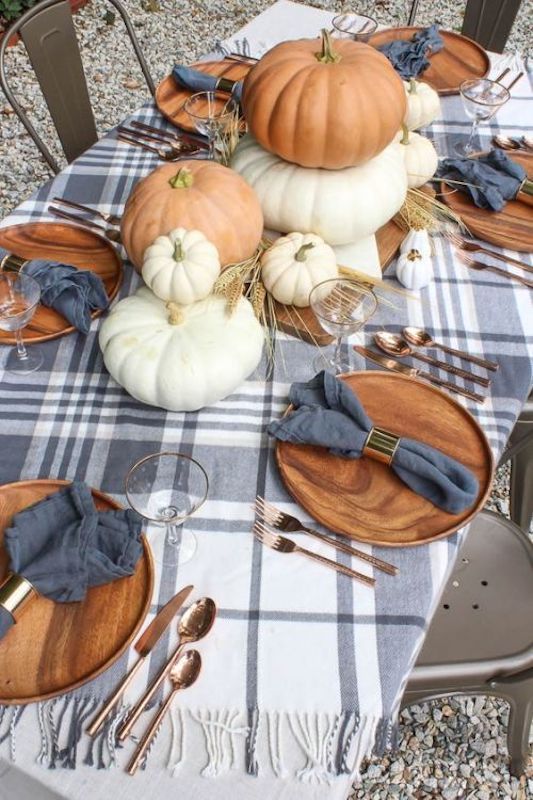 a lovely cozy Thanksgiving tablescape with a plaid runner, white and orange pumpkins, wheat, wooden chargers and copper cutlery