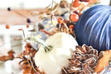 a lush Thanksgiving centerpiece of faux pumpkins, fall leaves berries, acorns and pinecones