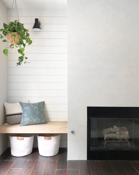 A minimalist farmhouse space with a built in fireplace, a built in seat wiht pillows and baskets under it is a lovely nook