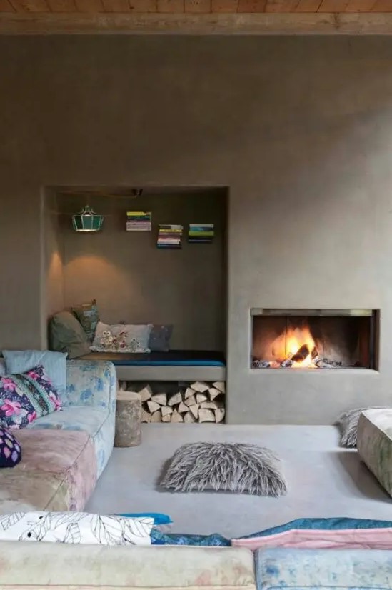 A minimalist fireplace nook with a built in hearth and a built in niche nook with books, a lamp and firewood under the bench is cozy