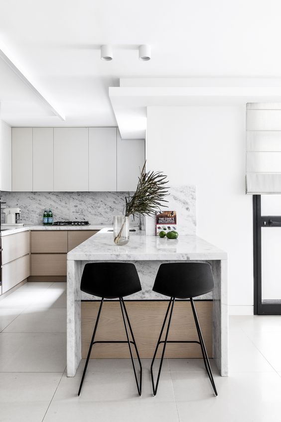 a minimalist kitchen with sleek grey and stained cabinets, a white marble backsplash and countertops, a small kitchen island with black stools