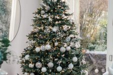 a modern Christmas tree styled with white, silver and clear ornaments and with lights and snowflakes is a chic idea