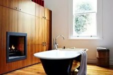 a modern bathroom with a wooden floor, a wooden storage unit that includes a fireplace, monograms and a black vintage bathtub