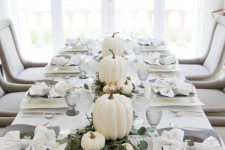 a modern elegant Thanksgiving tablescape with a greenery runner, white pumpkins, grey plates and glasses is very chic