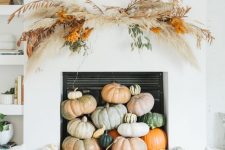 a modern fall or Thanksgiving fireplace filled with various natural pumpkins, with a pampas grass and greenery overhead decoration