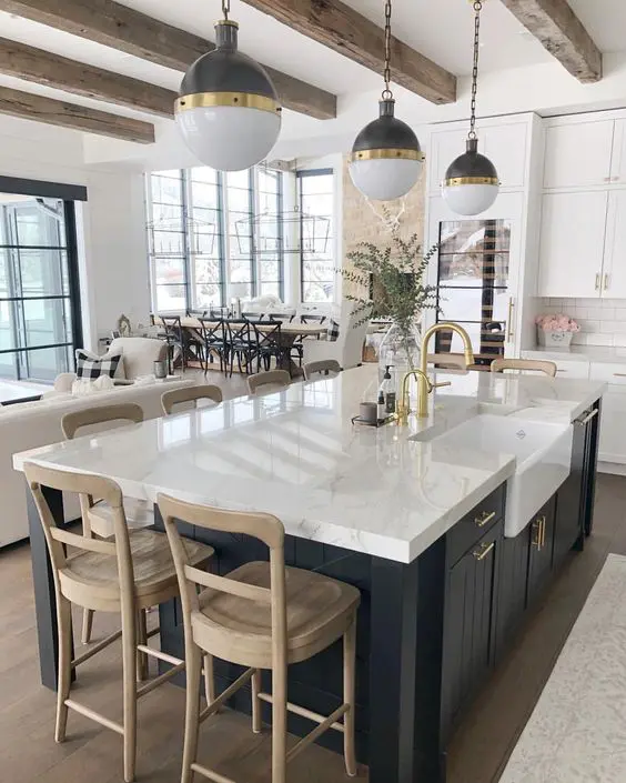 a modern kitchen with white cabinets, a navy kitchen island, stained stools and color block pendant lamps
