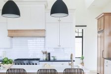 a modern kitchen with white shaker style cabinets, black countertops, a stained kitchen island and black metal stools